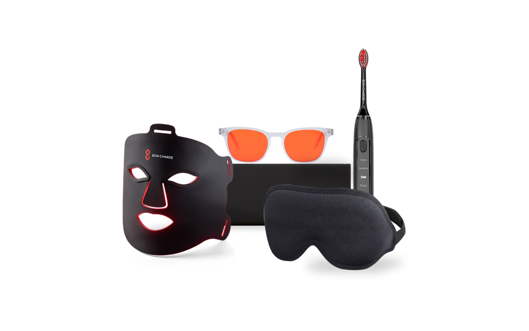 Face mask next to a black sleep mask, blue light blocking glasses with red lenses, and black electric toothbrush.